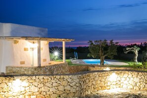 Un mur en pierre avec une piscine et un espace abrité agrémenté de luminaires.