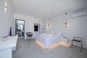 A modern, minimalist bedroom with a large bed, bedside tables, a chair, and a desk with a lamp.