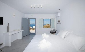 A modern bedroom with a large bed, a bedside table, a chair, and a view of the sea.