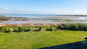 Un paysage côtier avec un premier plan herbeux, une plage de sable et un ciel bleu dégagé.