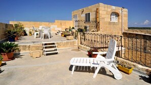 A rooftop terrace with outdoor furniture, potted plants, and a stone building with a balcony. - Discover Tranquility: rustic elegance in this beautifully converted farmhouse. (San Lawrenz)