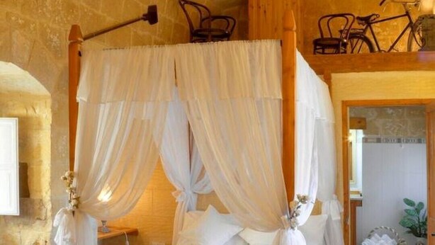 A four-poster bed with white drapes, a wooden chest, and a stone wall. - Discover Tranquility: rustic elegance in this beautifully converted farmhouse. (San Lawrenz)