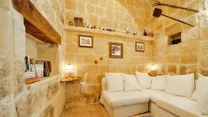 A cozy room with a stone wall, a wooden shelf with books, a white sofa, and a small table with a lamp. - Discover Tranquility: rustic elegance in this beautifully converted farmhouse. (San Lawrenz)
