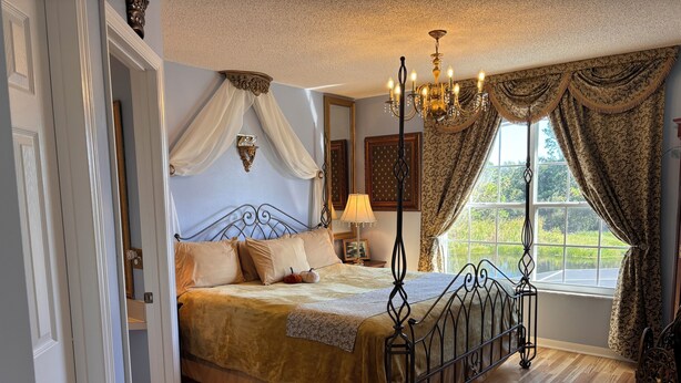 A bedroom with a four-poster bed, a chandelier, and a large window with curtains. - Disney Themed Home! Magic Kingdom Inspired!!  Hidden Mickeys!!! (Davenport)