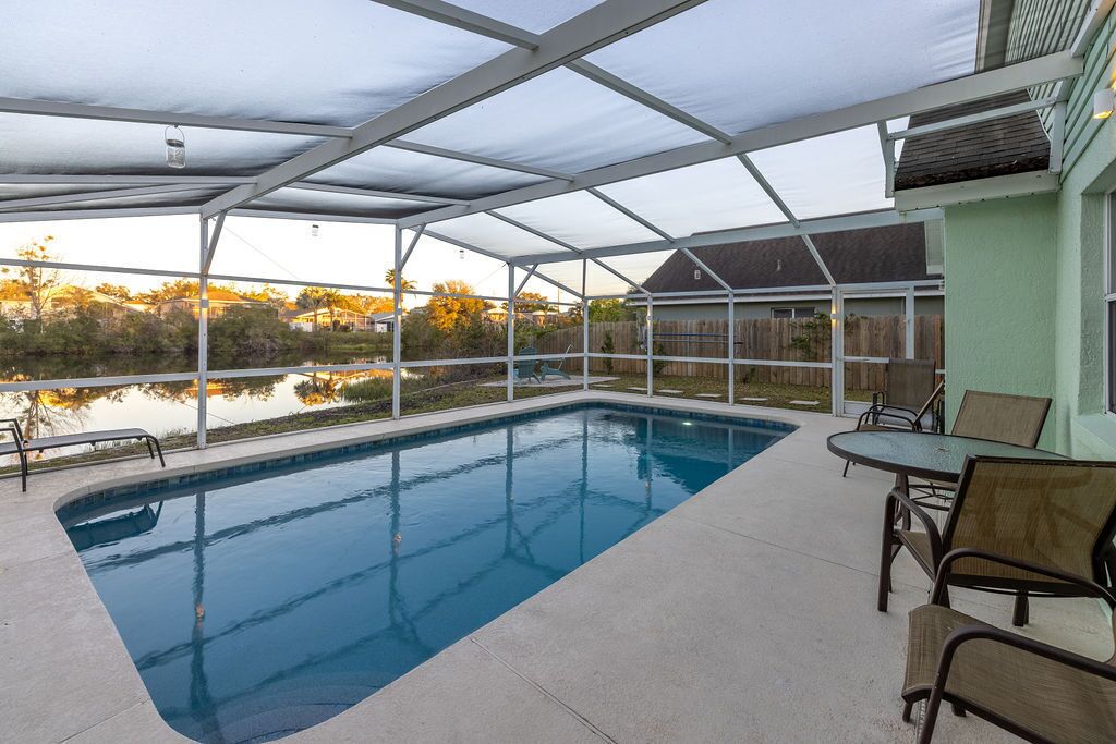 A covered outdoor swimming pool with a patio area, including chairs and a table.