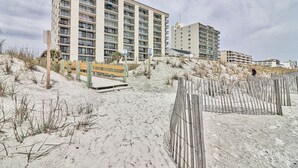 Un hotel frente a la playa con varios pisos, una playa arenosa y una valla de madera.
