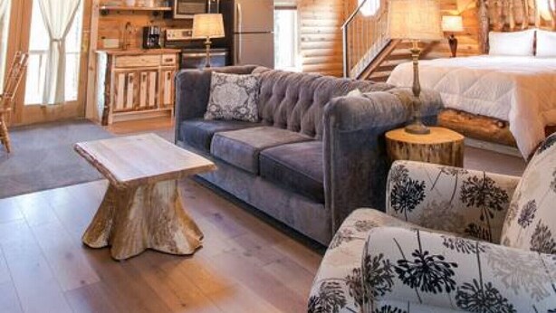 Ett rymligt rum i loftstil med högt i tak, synliga träbjälkar, en balkong, ett köksutrymme och en mysig sittgrupp med en soffa och fåtöljer.