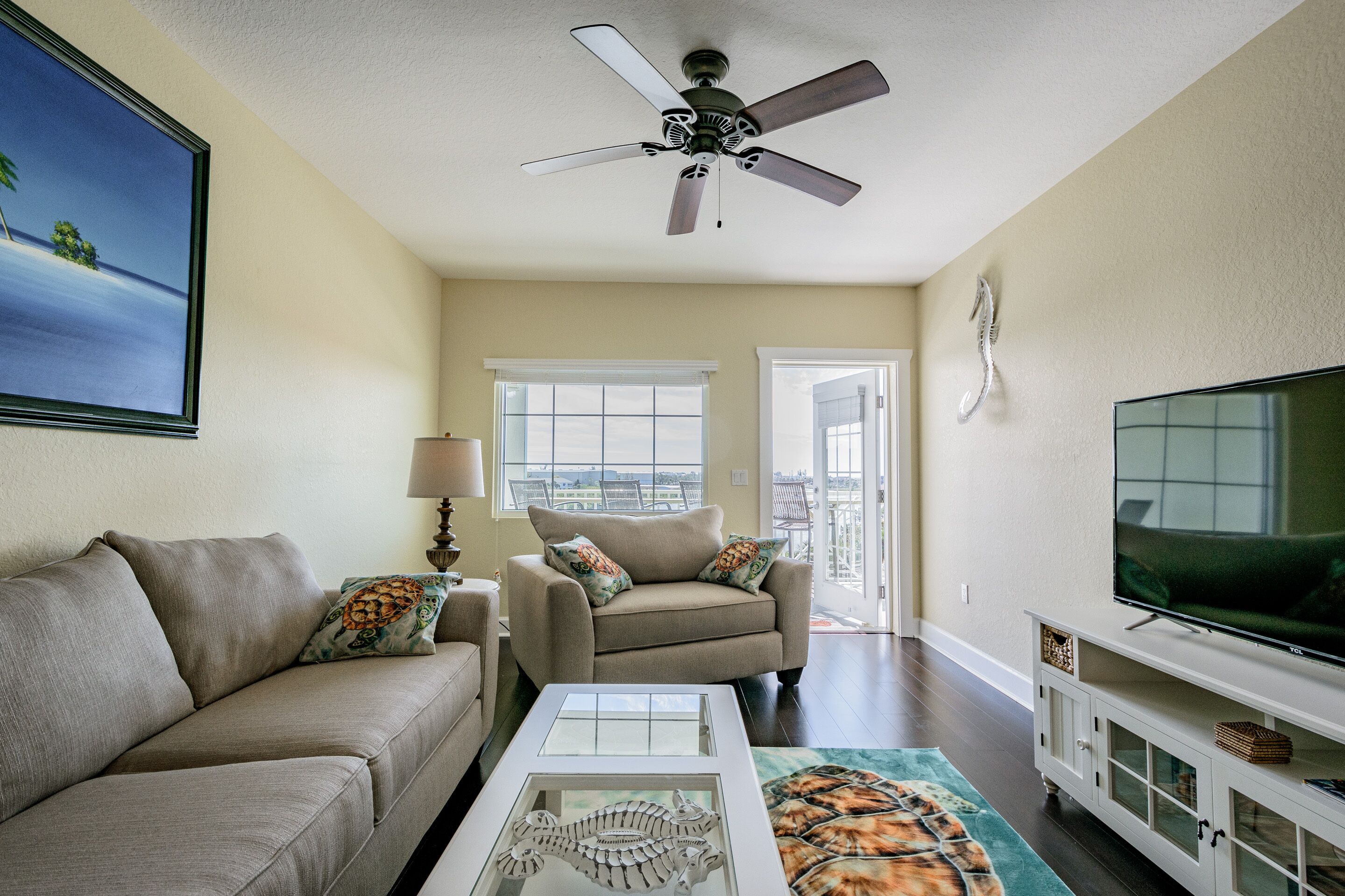 A living room with a beige sofa, a coffee table, a television, and a ceiling fan.
