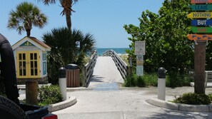 Un camino que lleva a una playa, con un cartel y un pequeño edificio que dice 'Indian Rocks Beach Free Library'.