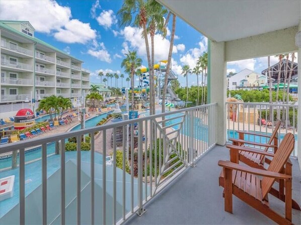 Un balcón de hotel con piscina, palmeras y vista a un parque acuático.
