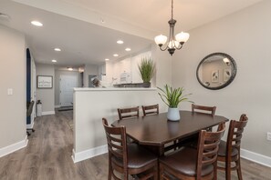 A dining area with a round wooden table, six chairs, a chandelier, a potted plant, and a mirror on the wall.