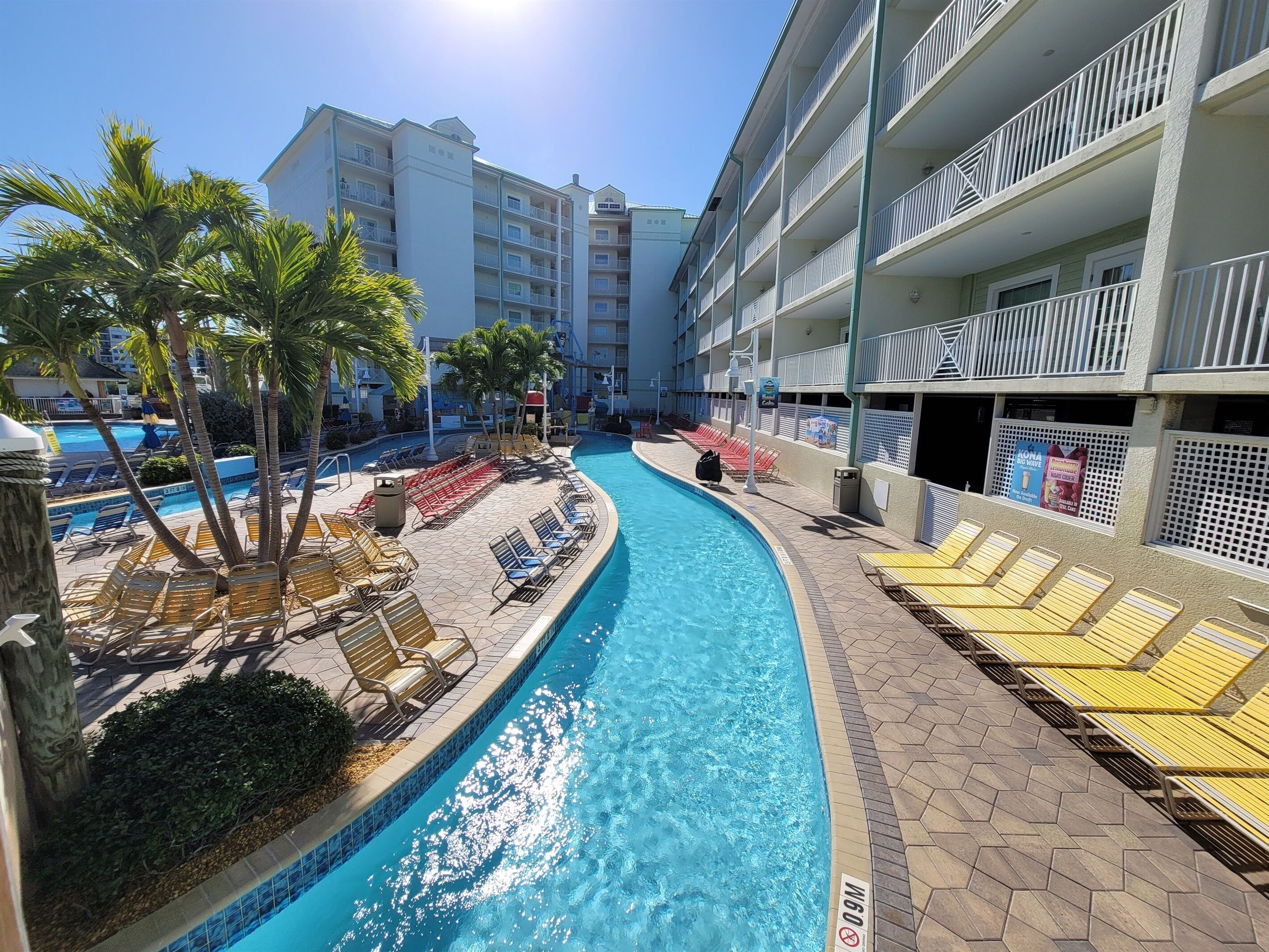 A hotel pool area with sun loungers, palm trees, and a clear blue pool.