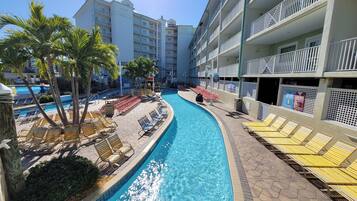 A hotel pool area with sun loungers, palm trees, and a clear blue pool.