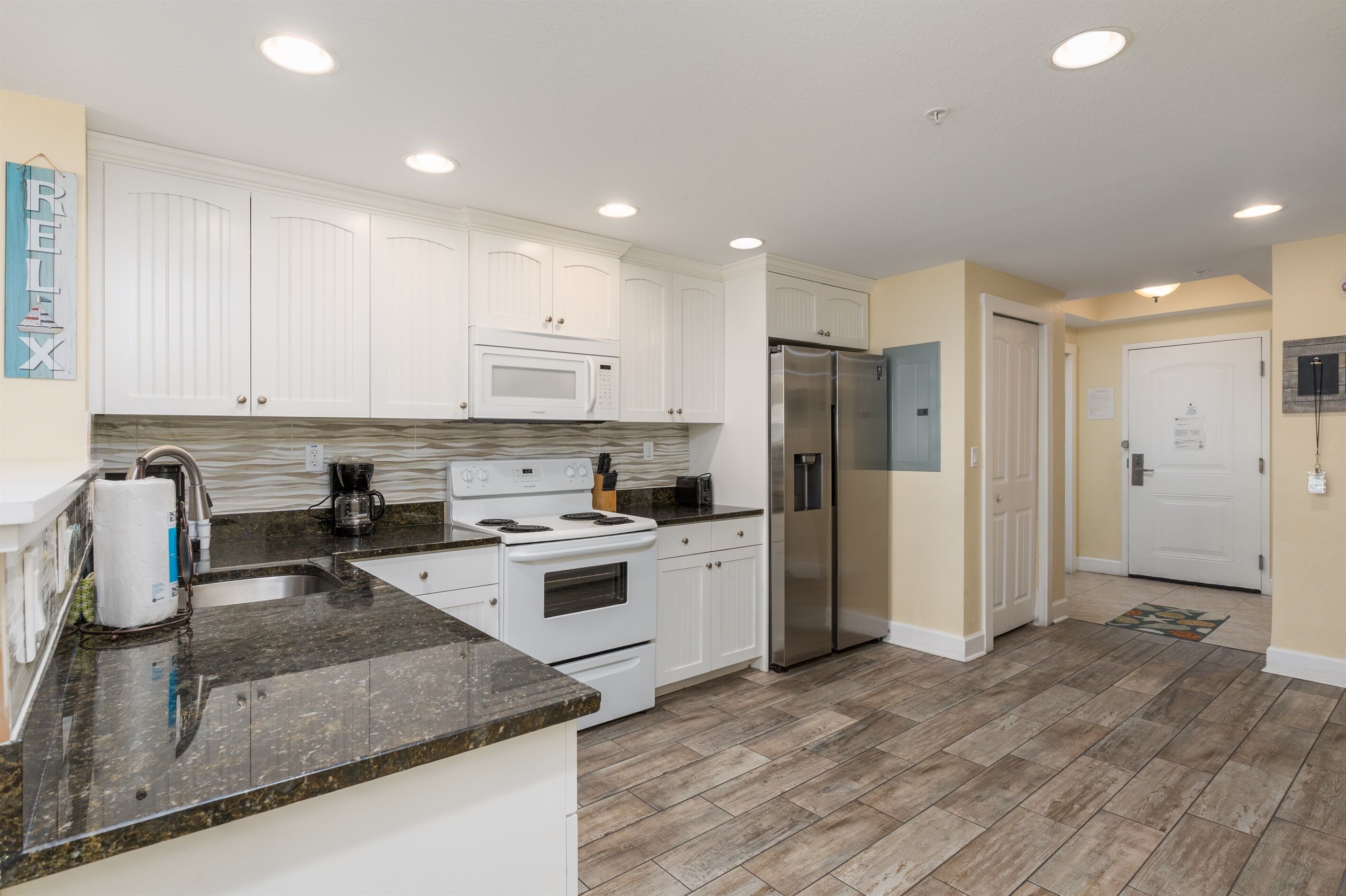 A modern kitchen with white cabinets, a stainless steel refrigerator, a built-in microwave, and a granite countertop.