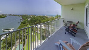 A balcony with a view of a river, chairs, and a table.