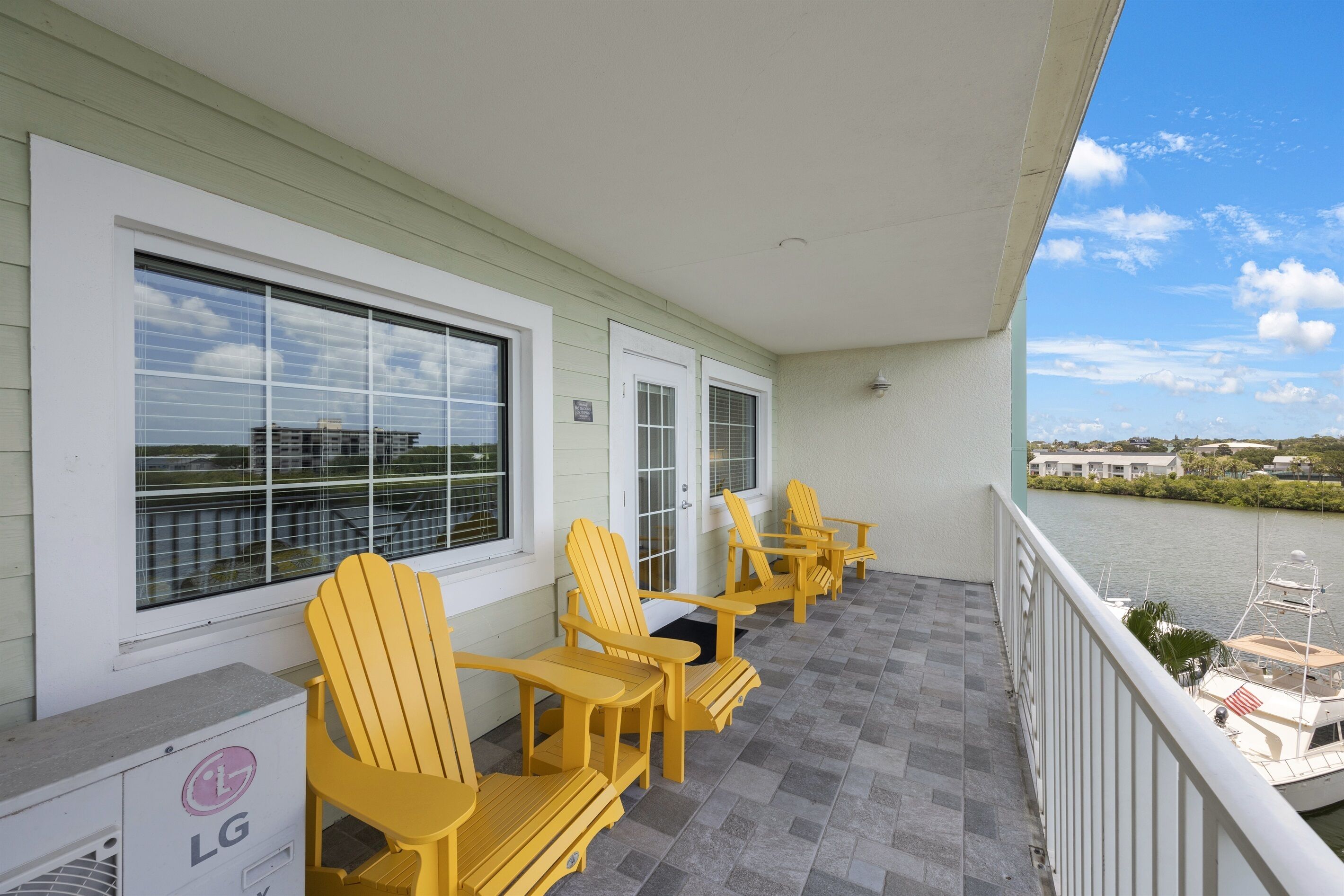 A balcony with yellow Adirondack chairs, a view of a river, and a boat docked nearby.