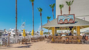 Un restaurant situé en bord de mer, avec une terrasse, des palmiers et des bateaux en arrière-plan.