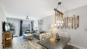 Una sala de estar moderna con una mesa de comedor, sofá y sillas. Hay un ventilador de techo, una lámpara y un adorno en la pared.