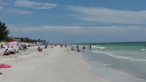 Relax on the beach with comfortable sun loungers and umbrellas, surrounded by a line of nearby accommodations.