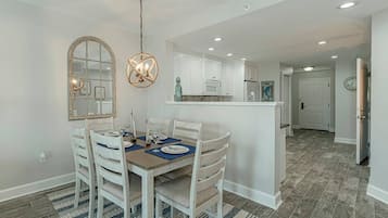 A dining area with a wooden table and white chairs, a kitchen with white cabinets, and a hallway leading to a door.