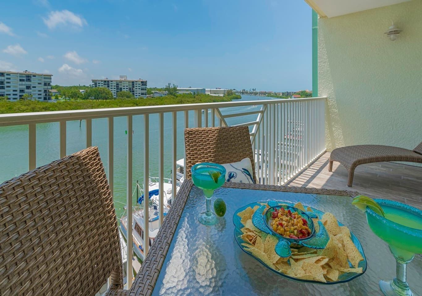 A balcony with wicker chairs, a glass table, a drink, and a bowl of chips.