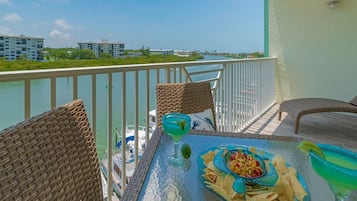 A balcony with wicker chairs, a glass table, a drink, and a bowl of chips.