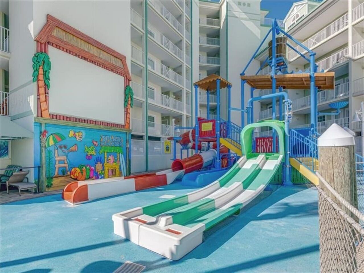A children's play area with slides and a pool, surrounded by a multi-level building with balconies.