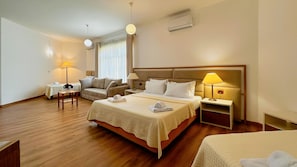 Quarto de hotel com cama, sofá, mesinha, abajur e aparelho de ar condicionado.