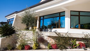 Una casa moderna con amplios ventanales, fachada de piedra y un pequeño patio con mobiliario exterior.