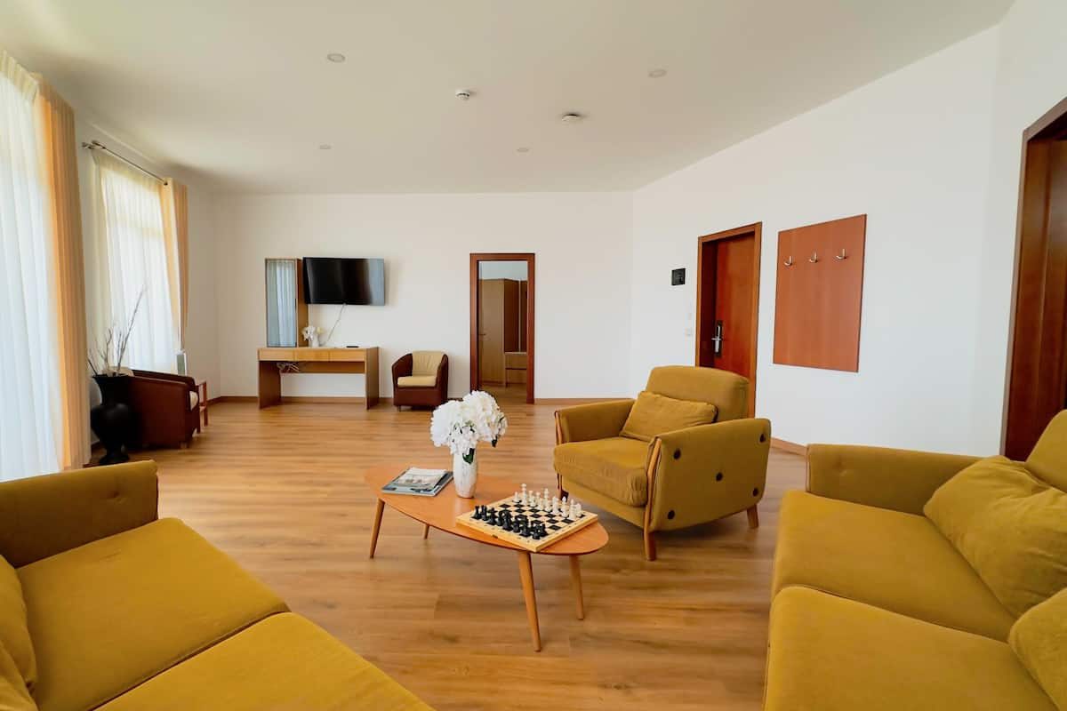 Ein Wohnzimmer mit gelben Sofas, einem Couchtisch mit Schachspiel, einem Fernseher und einem Schreibtisch.