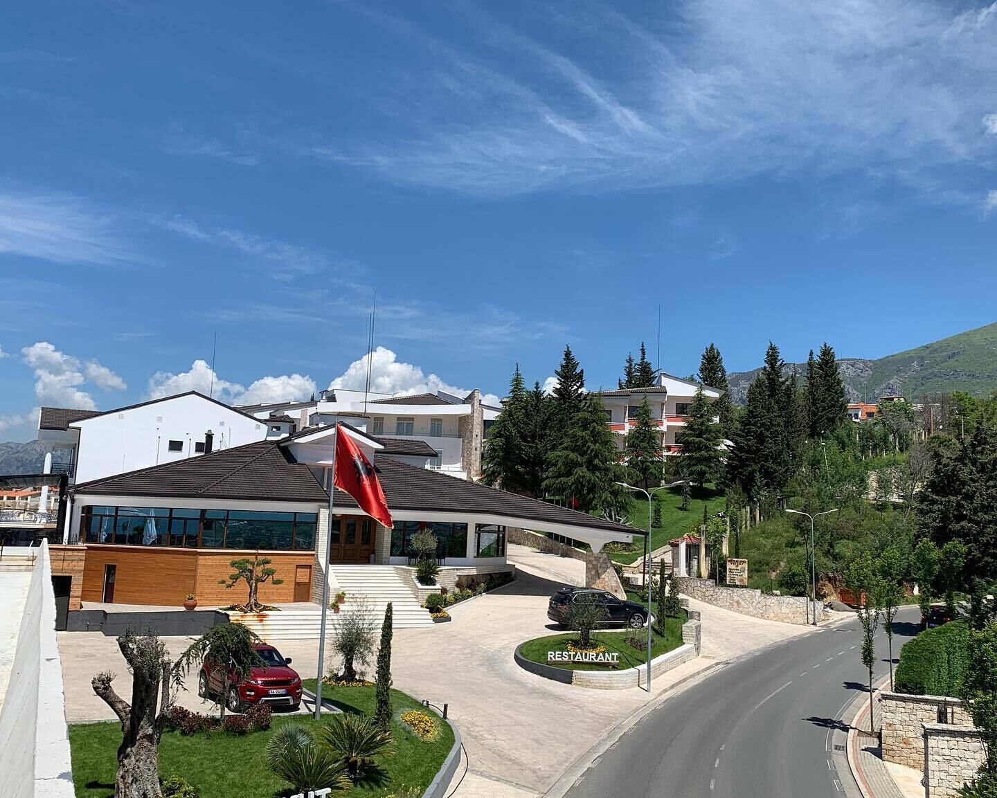A modern building with a flag, a restaurant sign, and a road curving around it.