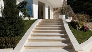 Un edificio moderno con fachada curva, revestimiento de piedra y un conjunto de escalones amplios que conducen a una puerta.
