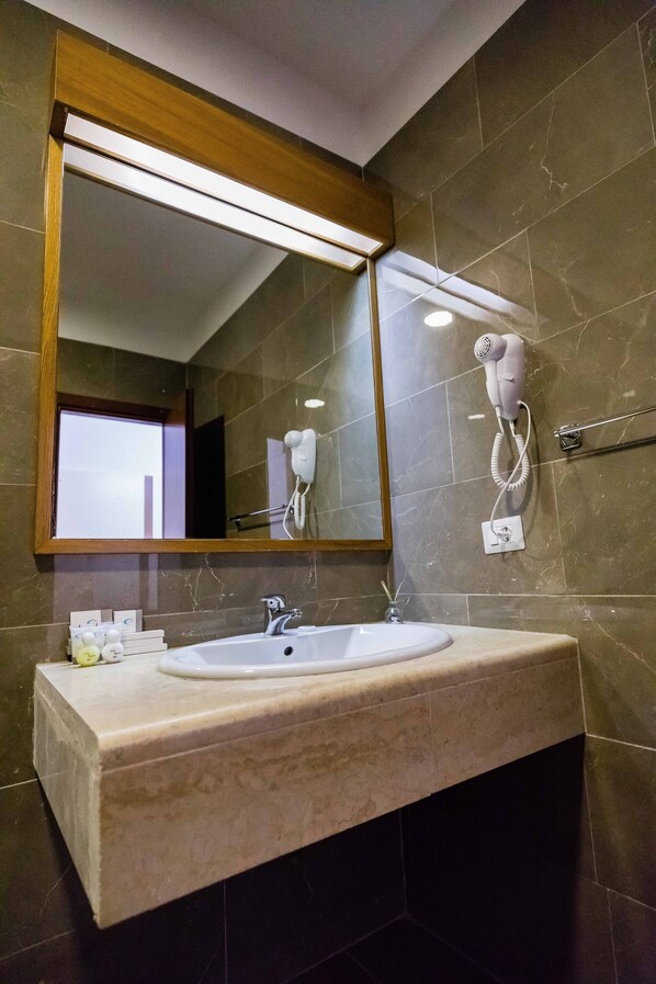 Une salle de bain dotée d’un grand miroir, d’un sèche-cheveux fixé au mur, d’un lavabo avec un plan de travail en marbre et d’un porte-serviettes.