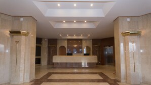 Un vestíbulo amplio con un mostrador de recepción central, techos altos y un diseño geométrico en el techo.