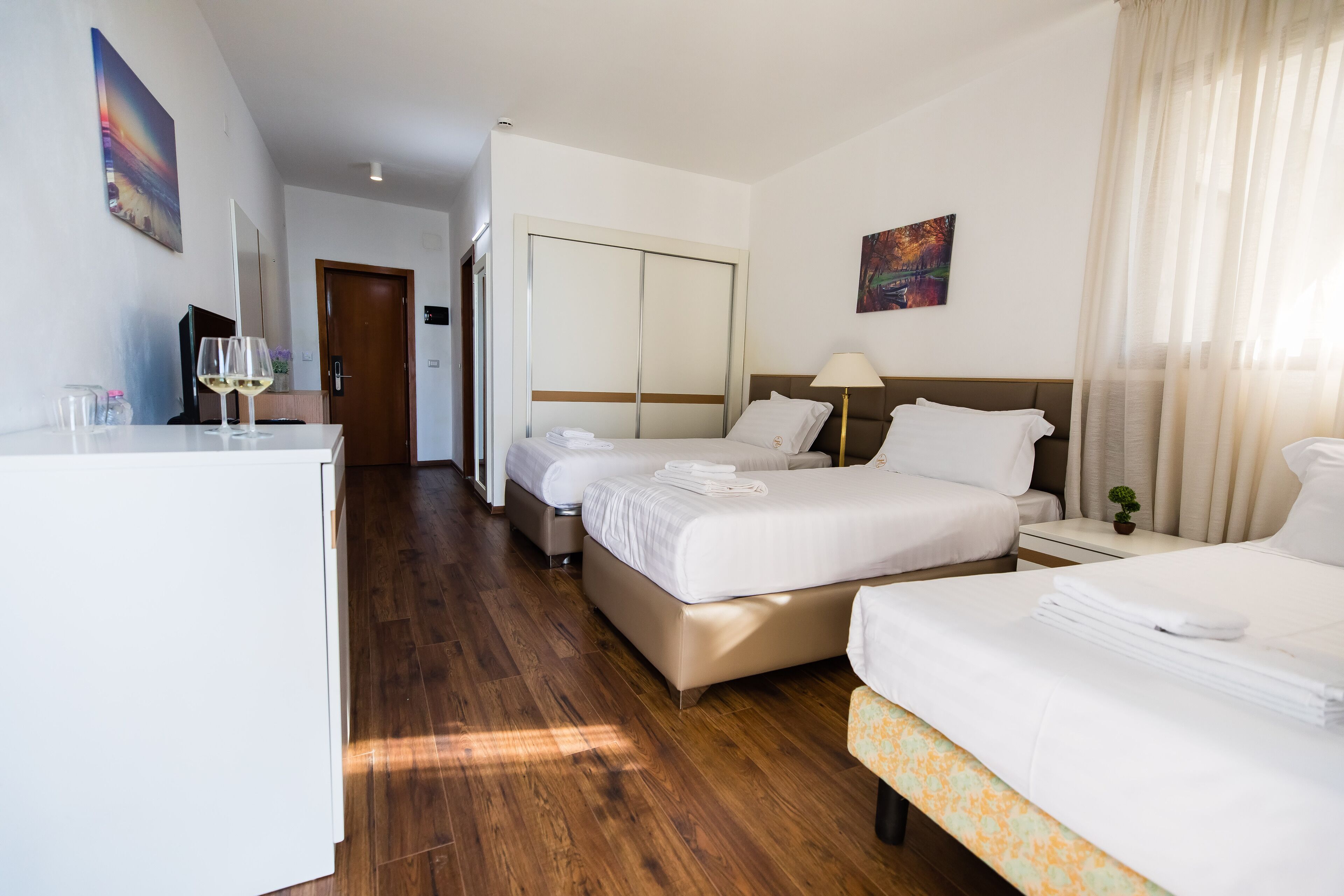 A hotel room with two beds, a desk, a chair, a lamp, and a small plant.