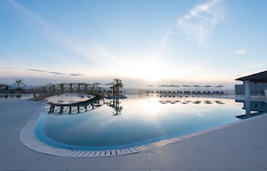 Une piscine aux eaux cristallines, avec un pont en bois, des chaises longues et des parasols, le tout sous un ciel dégagé.