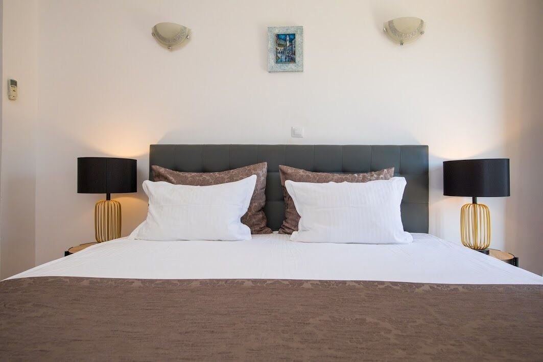 A neatly made bed with white and brown pillows, two bedside lamps, and a framed picture on the wall.