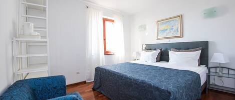 Una habitación de hotel con una cama, una silla, una estantería y un cuadro en la pared.