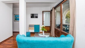 A modern living room with a blue sofa, a wooden cabinet, and a large window with curtains. - Villa Dard (Dubrovnik)