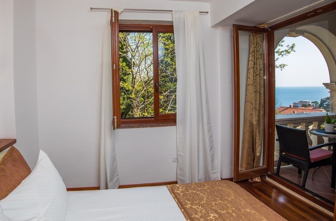 A bedroom with a bed, a window with curtains, and a view of the sea through an archway.