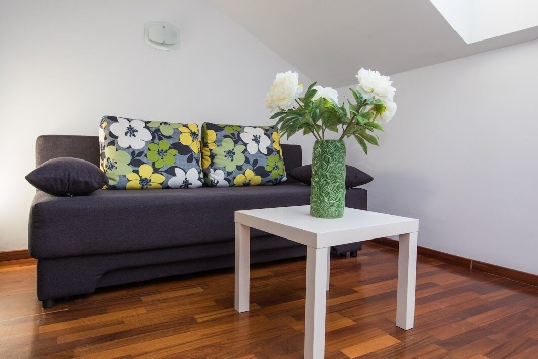 Ett modernt vardagsrum med en mörkgrå soffa, blommiga kuddar, ett vitt soffbord och en grön vas med vita blommor.