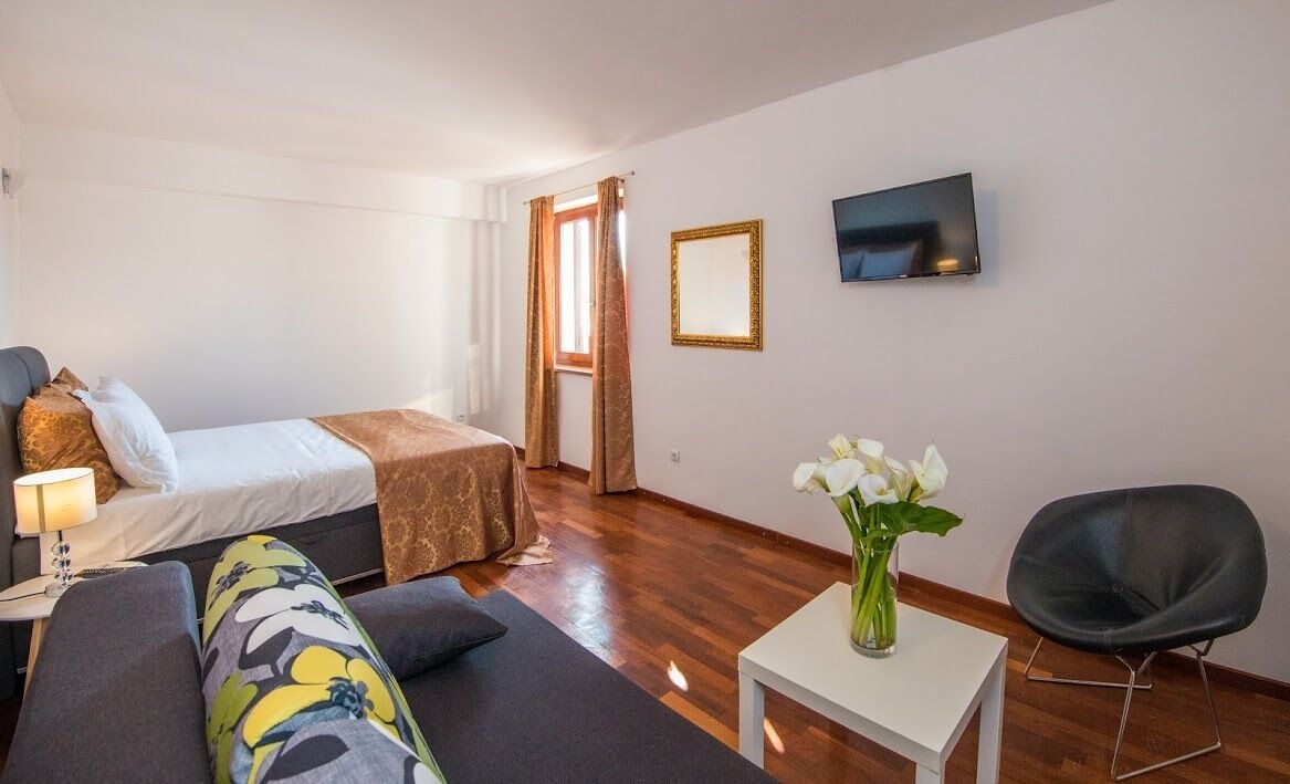 A hotel room with a bed, a sofa, a TV, a small table with a vase of flowers, and a chair.