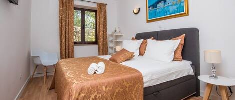 Une chambre d’hôtel avec un lit, un bureau, une chaise, une fenêtre avec des rideaux, un tableau au mur et une lampe sur une table de chevet.