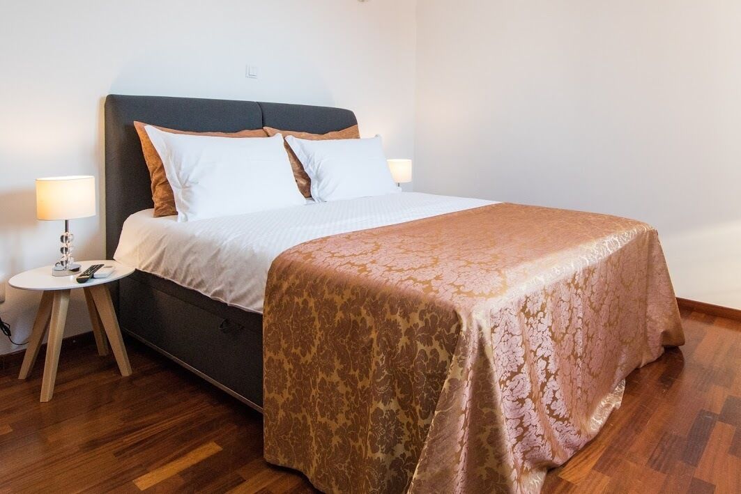 A neatly made bed with a patterned bedspread, a bedside table with a lamp, and a wall socket.