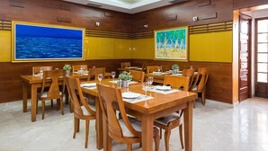 A conference room with wooden tables and chairs, large windows with ocean and forest paintings, and a polished floor. - Villa Dard (Dubrovnik)