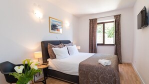 A bedroom with a bed, bedside table, lamp, artwork, and a window with curtains. - Villa Dard (Dubrovnik)