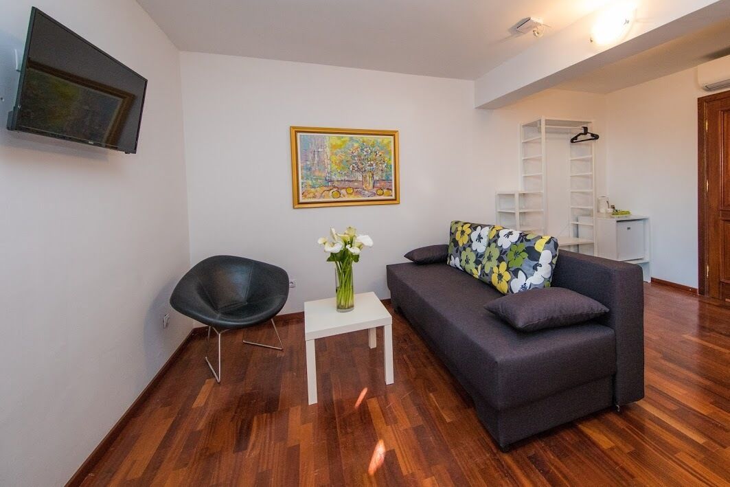 Een moderne woonkamer met een grijze bank, een zwarte stoel, een klein wit tafeltje met een bloevas en een schilderij aan de muur.