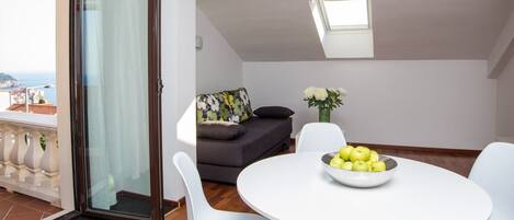 A modern living room with a round white table, a grey sofa, and a glass door leading to a balcony.