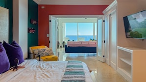 Une chambre à coucher avec un lit, une chaise et une vue sur l’océan par une grande fenêtre.