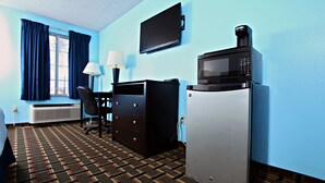 Camera d'albergo con TV a schermo piatto, forno a microonde, frigorifero, scrivania con sedia, lampada e tappeto decorato.